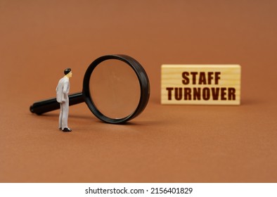 Business concept. A figurine of a businesswoman looks through a magnifying glass at a block with the inscription - Staff Turnover. Block blurred
