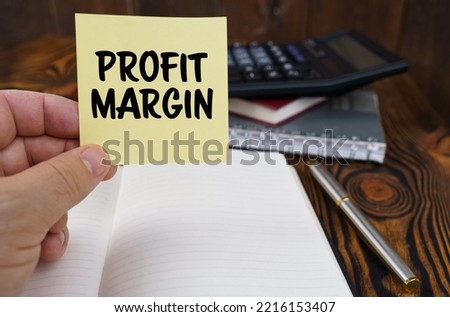 Business concept. In the hands of a man is a sticker with the inscription - PROFIT MARGIN. In the background in a blurred background are office items.