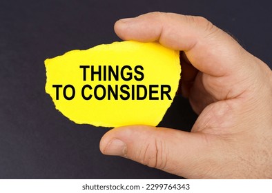 Business concept. On a black background, in the hands of a man, a yellow torn cardboard with the inscription - Things To Consider - Shutterstock ID 2299764343