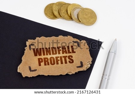 Business concept. On a black and white surface lies a pen, coins and a cardboard sign with the inscription - Windfall profits