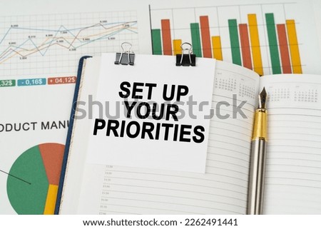 Business concept. On the business charts lies a pen, a notepad with note paper with the inscription - SET UP YOUR PRIORITIES Foto d'archivio © 