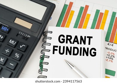 Business concept. On business charts there is a calculator, a pen and a notepad with the inscription - GRANT FUNDING