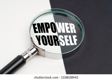 Business concept. On the surface, which is half black and white, lies a magnifying glass inside which is written - EMPOWER YOURSELF