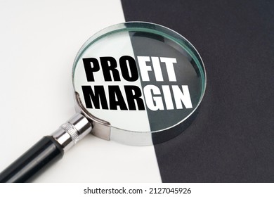 Business concept. On the surface, which is half black and white, lies a magnifying glass inside which is written - PROFIT MARGIN - Shutterstock ID 2127045926