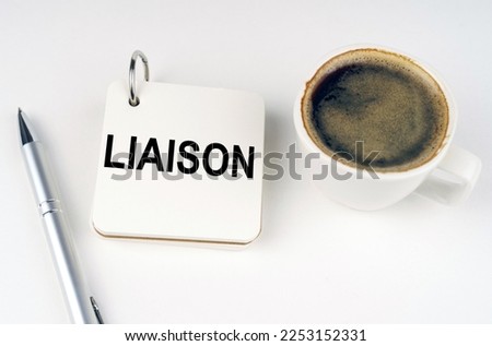 Business concept. On a white surface, a cup of coffee, a pen and a notepad with the inscription - LIAISON