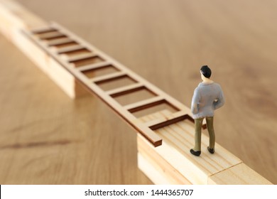 business concept picture of challenge. A man stands on the edge of a high wall and passes the gap by placing a ladder. Problem solving and decisionmaking.