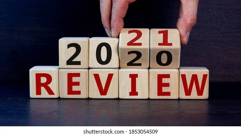 Business concept of planning 2021. Male hand flips wooden cubes and changes the inscription 'Review 2020' to 'Review 2021'. Beautiful dark wooden background, copy space.