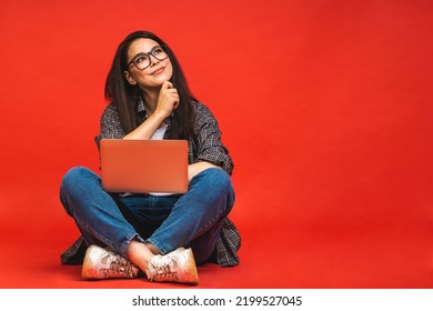Business concept. Portrait of happy brunette woman in casual sitting on floor in lotus pose and holding laptop isolated over red background. - Shutterstock ID 2199527045