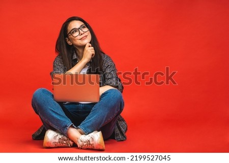 Business concept. Portrait of happy brunette woman in casual sitting on floor in lotus pose and holding laptop isolated over red background.