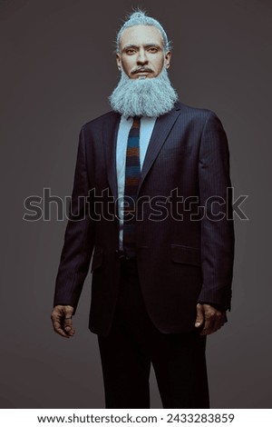 Business concept. A respectable man with a gray hairstyle and a beard in Japanese style, dressed in an elegant suit, looks calmly and confidently into the camera. Gray studio background.