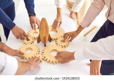 Business concept. Team of cropped company employees join gearwheels around toy rocket as metaphor for unity, teamwork, choosing new effective strategy and launching new project