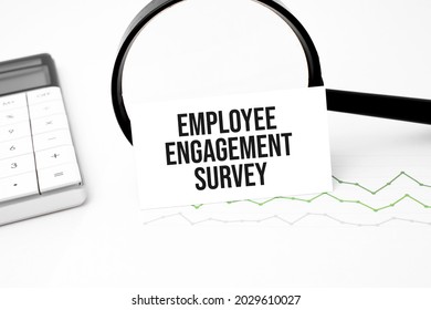 Business Concept. Top View Of Calculator, Magnifier, Pen, Table Clock And Notebook Written Employee Engagement Survey On Wooden Background.