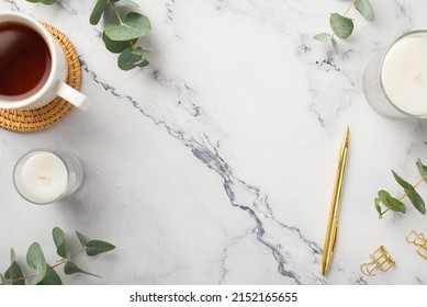 Business concept. Top view photo of candles cup of tea on rattan serving mat gold pen binder clips and eucalyptus on white marble background with copyspace