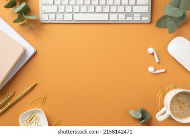 Business concept. Top view photo of workplace white keyboard computer mouse notepads wireless earbuds gold pen clips cup of coffee and eucalyptus leaves on isolated orange background with empty space