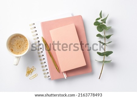 Business concept. Top view photo of workplace stack of pink diaries cup of coffee clips gold pen and eucalyptus sprig on isolated white background