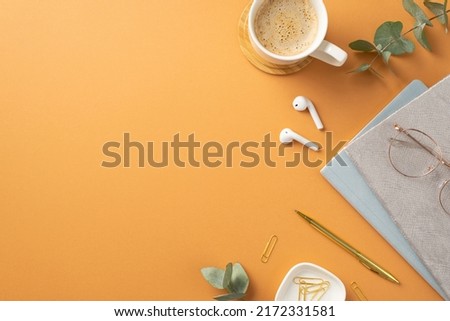Business concept. Top view photo of workspace cup of coffee on wooden stand wireless earbuds glasses diaries gold pen clips eucalyptus on isolated orange background with copyspace