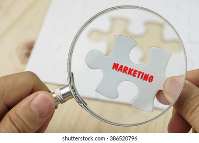 Business concept.Hand with magnifying glass searching for a piece of jigsaw puzzle with MARKETING word. - Shutterstock ID 386520796