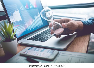 Business concepts with businessman holding hourglass with graph chart on computer laptop.For investment analysis,Waiting to sucess ideas