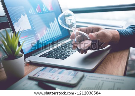Business concepts with businessman holding hourglass with graph chart on computer laptop.For investment analysis,Waiting to sucess ideas