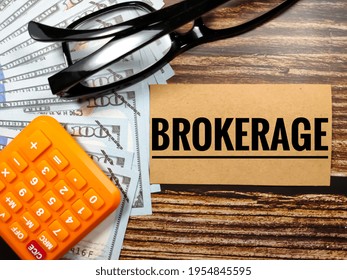 Business Concept.Text BROKERAGE With Glasses,banknote And Blur Calculator On A Brown Wooden Background.