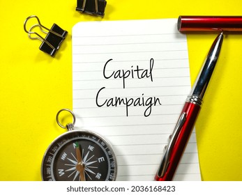 Business Concept.Text Capital Campaign Writing On Notepaper With Pen,paper Clips And Compass On Yellow Background.