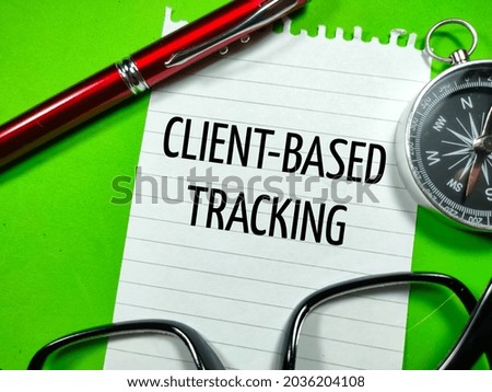 Business concept.Text CLIENT BASED TRACKING writing on notepaper with glasses,compass and pen on green background.
