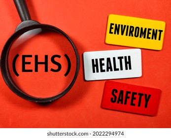 Business concept.Text EHS (Enviroment Health Safety) writing on colored wooden board with magnifying glass on red background