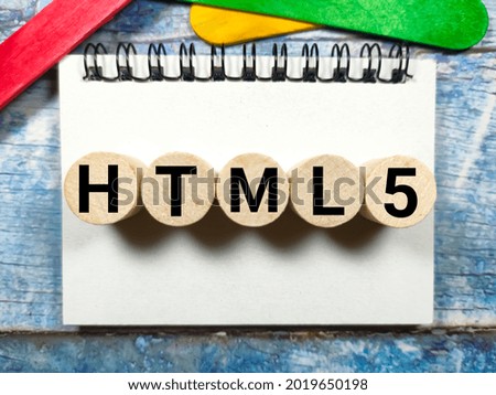 Business concept.Text HTML5 writing on block cylinder  with notebook and colored ice cream sticks on a wooden background.