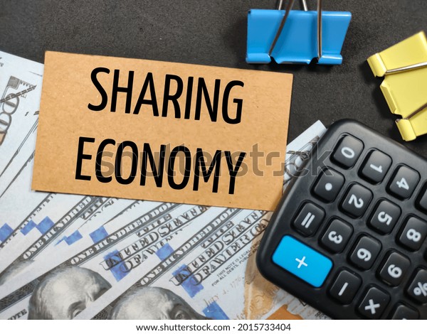 Business concept.Text SHARING ECONOMY writing
on brown card with dollar money,paper clips and calculator on a
black background.