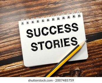 Business Concept.Text SUCCESS STORIES On Notebook With Pencil On A Wooden Background.