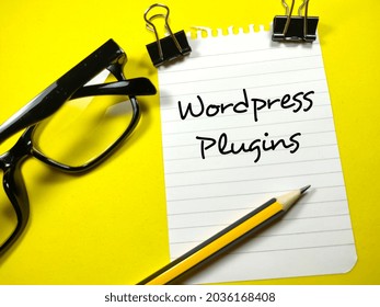 Business concept.Text Wordpress Plugin writing on notepaper with pencil,paper clips and glasses on yellow background.