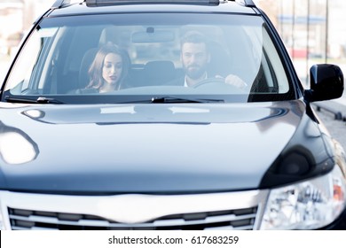 Business Couple Having A Conversation While Driving A Car. Front View Through The Windshield