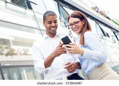 Business Couple Looking At Smart Phone And Smiling. Shallow Depth Of Field.