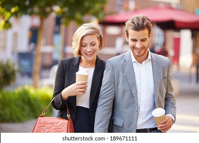 Business Couple Walking Through Park With Takeaway Coffee