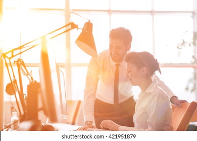 Business Couple Working Together On Project At Modern Startup Office. Early Morning Scene With Sun Flare In Background