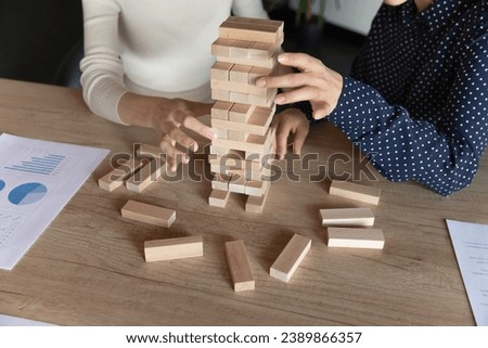 Business coworkers playing jenga at work table, removing wooden blocks from toy building tower, having fun with board game. Teambuilding, teamwork, cooperation concept. Close up