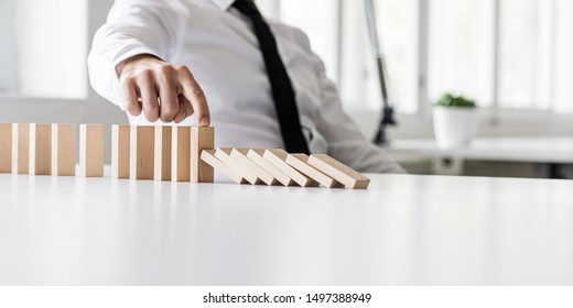 Business crisis manager preventing wooden dominos to collapse in a conceptual image.