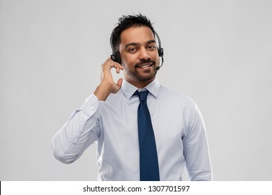 business, customer service and people concept - smiling indian businessman or helpline operator in headset over grey background