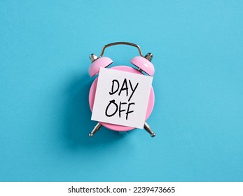 Business Day Off Annual Leave, Relaxation, Holiday or Vacation Concept. Pink alarm clock with a note paper on blue background with the message day off.
