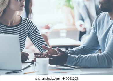 Business Discussion. Close-up Of Two Young Business People Discussing Something While Sitting At The Office Desk Together While Their Colleagues Sitting In The Background