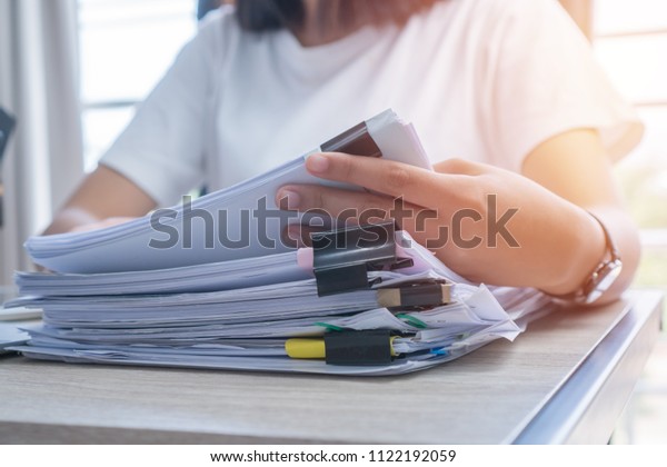 Business Documents concept : Employee woman hands\
working in Stacks paper files for searching and checking unfinished\
document achieves on folders papers at busy work desk office. Soft\
focus