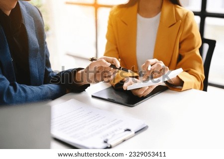 Business documents on office table with smart phone and laptop and two colleagues discussing data in the background 