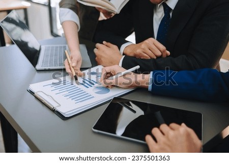 Business documents on office table with smart phone and laptop and two colleagues discussing data in the background 
