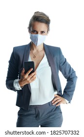 Business During Covid-19 Pandemic. Modern Middle Aged Business Woman In A Grey Suit With Medical Mask Using Smartphone Applications Against White Background.