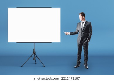 Business Education Concept With Businessman Front View With Chalk In Right Hand Near Blank White Flip Chart With Place For Your Logo Or Text In Abstract Room On Blue Wall Background, Mock Up