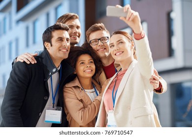 Business, Education And Corporate Concept - International Group Of People With Conference Badges And Smartphone Taking Selfie On City Street