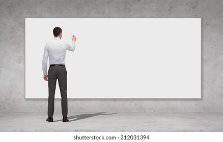 Business, Education And Office People Concept - Businessman Or Teacher With Marker Writing Or Drawing Something On White Blank Board Over Concrete Wall Background From Back