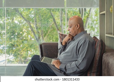 Business Elderly Black American Man, African Person Working From Home, Thinking About Problem With Computer Notebook Laptop And Suffering From Depression In Quarantine In Corona Virus Pandemic Concept