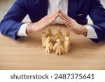 Business employer executive manager protecting rights of employees. Man holding hands over group of small little wooden human doll figures on table. Metaphor for care, protection and safety at work