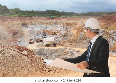 Business Engineer Planing At Construction Site With Workers On A Background Of Coal Mining Trucks Are Driving On The Road.